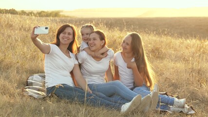 happy family travels, selfie on smartphone in park. mom and healthy children are sitting on blanket. mother with her daughters is photographed in field on blanket. family travel and adventure concept