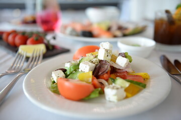 Greek salad on white plate with other dishes on the background 
