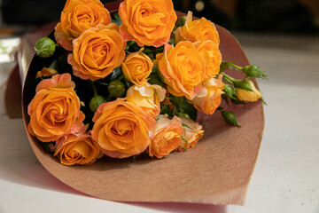 A festive bouquet of yellow-orange roses is Packed in Burgundy paper on a marble background