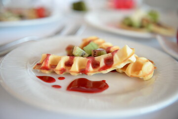 Waffles with red berry Compote and sliced kiwi on a white plate on a white table cloth 