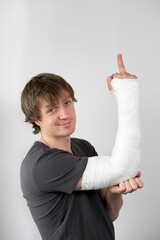 Attractive young man with plaster cast on his hand showing sing fuck you on a white wall background.