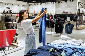 Cheerful woman choosing jeans in clothing store