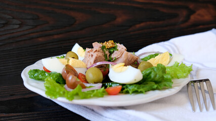 Tuna salad with eggs and olives, cherry tomato, cucumber, and onion on the wood background