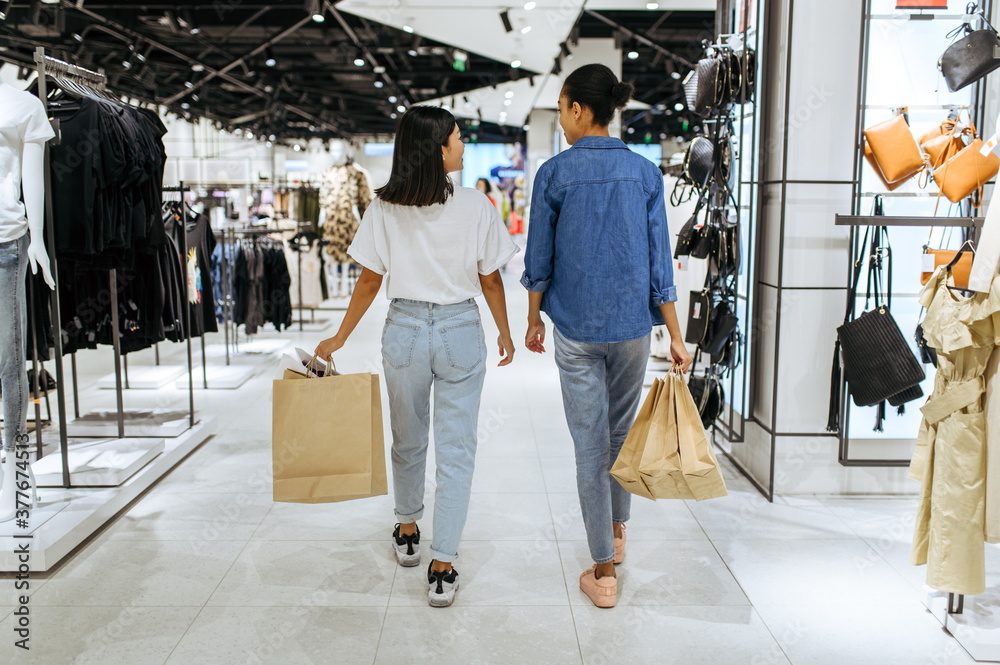 Wall mural girlfriends with bags walks in clothing store