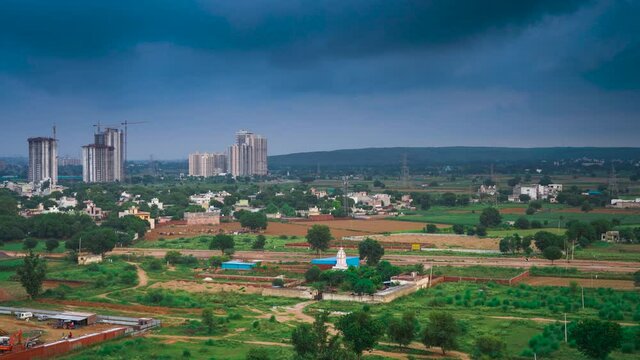 Aerial timelapse of dusk in gurgaon delhi cityscape with monsoon clouds casting shadows on high rise apartments and buildings with the aravali mountain hill range in the distance