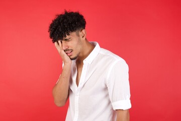 Young arab man with afro hair wearing shirt standing over isolated red background  Yawning tired covering half face, eye and mouth with hand. Face hurts in pain.