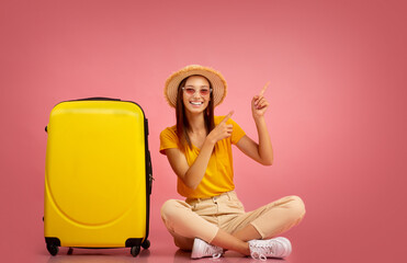 Summer girl sitting next to suitcase, pointing aside