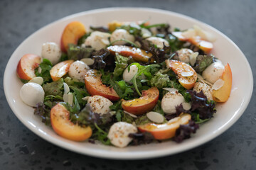 Closeup salad with nectarines, mozzarella and mixed greens in white plate on concrete background