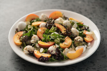 Closeup salad with nectarines, mozzarella and mixed greens in white plate on concrete background