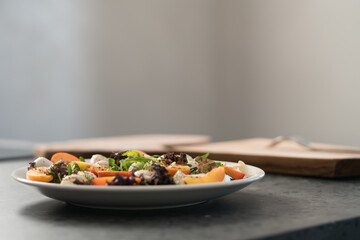 Closeup salad with nectarines, mozzarella and mixed greens in white plate on concrete countertop