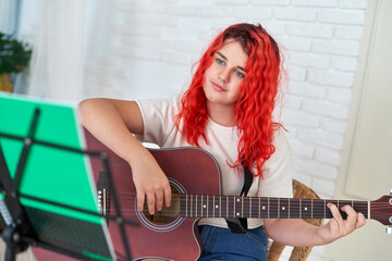 Teenage girl learns to play the guitar and looks at the textbook with chords