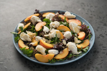 salad with nectarines, mozzarella and mixed greens in blue plate on concrete background