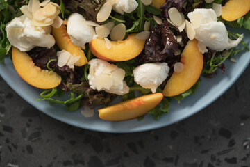 salad with nectarines, mozzarella and mixed greens in blue plate on concrete background from above