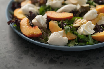 salad with nectarines, mozzarella and mixed greens in blue plate on concrete background