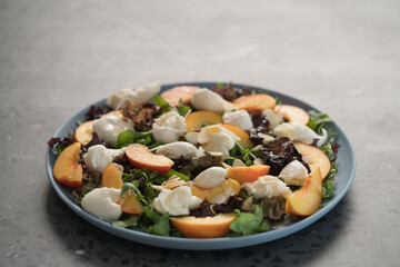 salad with nectarines, mozzarella and mixed greens in blue plate on concrete background with copy space