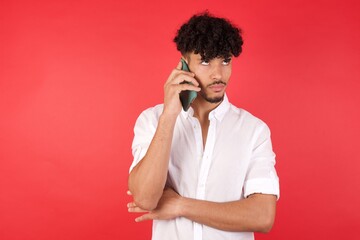 Sad Young arab man with afro hair wearing shirt standing over isolated red background talking on smartphone  Communication concept.