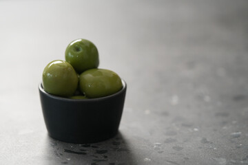 big green olives in black bowl on concrete background