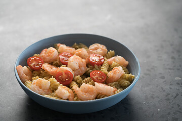Fusilli with shrimps, cherry tomatoes and pesto in a blue bowl on concrete background