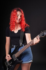 Obraz premium A teenage girl of the age of 12 years old plays an electric guitar while smiling on a black background
