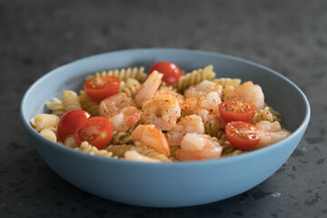 Fusilli with shrimps, cherry tomatoes and pesto in a blue bowl on concrete background
