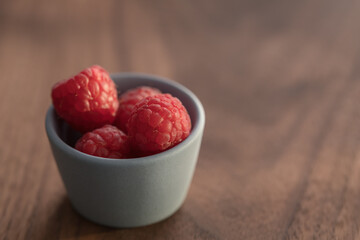Fresh ripe raspberries in small blue bowl on walnut wood background