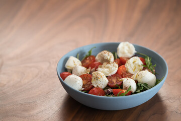 Salad with mozxarella, tomatoes and arugula in a blue bowl on walnut wood table