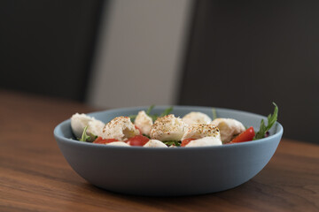 Salad with mozxarella, tomatoes and arugula in a blue bowl on walnut wood table