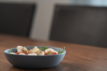 Salad with mozxarella, tomatoes and arugula in a blue bowl on walnut wood table