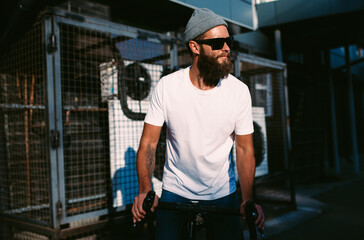 Fototapeta na wymiar Young bearded hipster guy wearing white blank t-shirt ride on bicycle . Mock-up for print. T-shirt template.