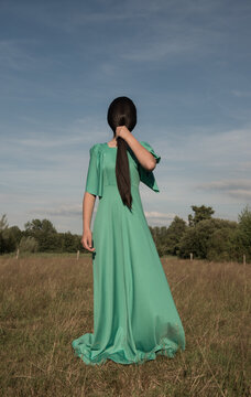 Teenage girl in green dress holding her black hair in ponytail in field