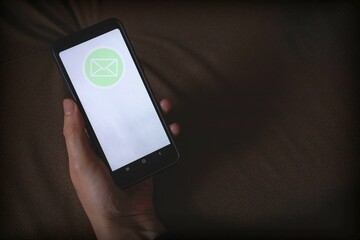 Smartphone mockup. A hand holds a black telephone with a white screen and mail icon. Copy space