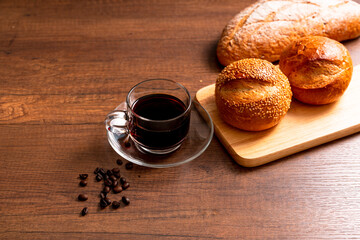 Glass Cup of hot black coffee with bread on wood background