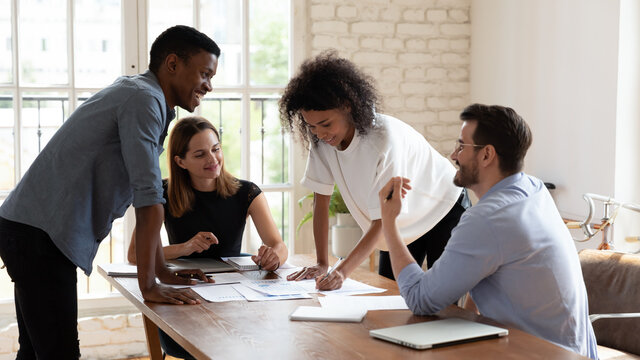 Happy multiethnic businesspeople brainstorm discuss paperwork stats report at meeting together, smiling diverse multiracial colleagues talk negotiate with at office briefing, collaboration concept