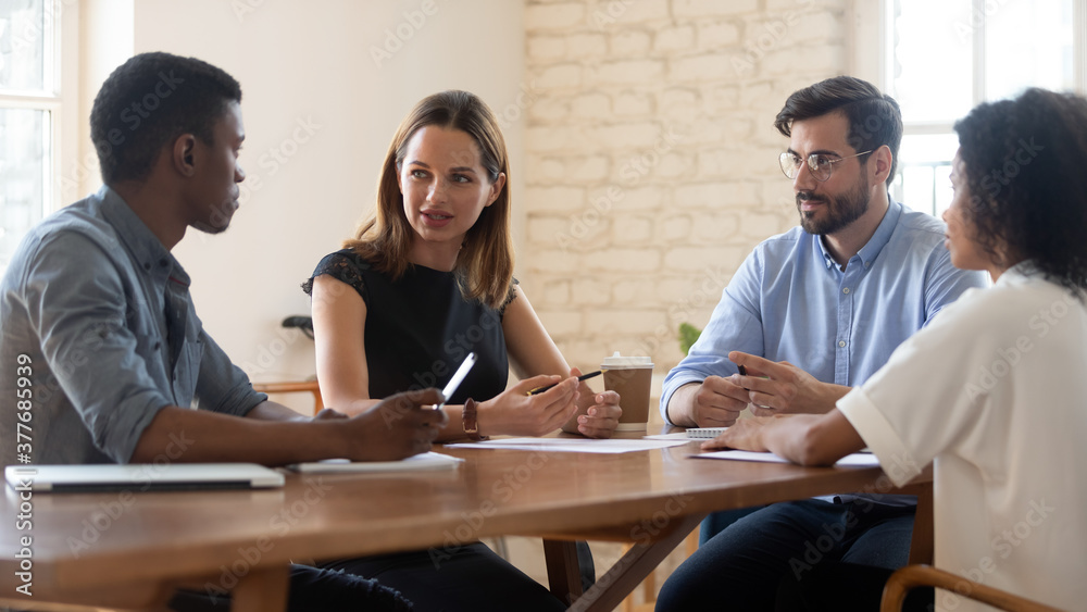 Wall mural young multiethnic colleagues sit at desk talk discuss ideas at work meeting in office, concentrated 