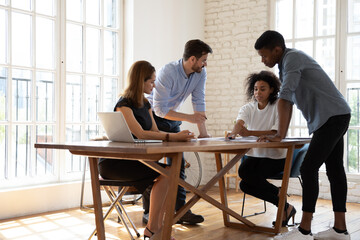 Concentrated diverse multiracial businesspeople sit at desk in office discuss paperwork at briefing together, focused multicultural colleagues brainstorm cooperate at meeting, collaboration concept