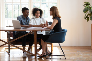 Young African American husband and wife sit at desk talk with female real estate agent discuss buying house together, biracial couple meet with designer architect or broker consult in modern office - Powered by Adobe