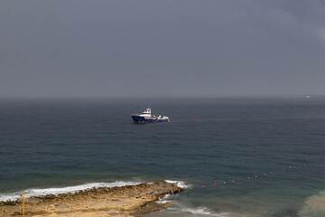 Sliema coastline with beach stone, Malta. sea view with boat. bad weather at sea