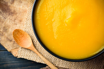 Close up of pumpkin soup in a bowl with spoon on wooden table, Top view