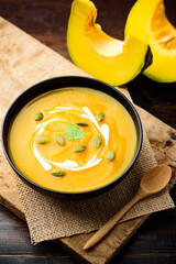 Pumpkin soup in a bowl with spoon and fresh pumpkins on wooden table