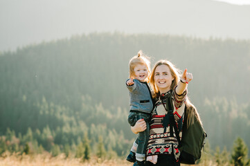 Mom with backpack and child walk in the autumn grass. The daughter and mother walking on nature. Family spending time together in mountain on vacation. Holiday trip concept. World Tourism Day.
