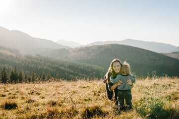Fototapeta na wymiar The daughter hug parent on nature. Mom with backpack and child walk in the autumn grass. Family spending time together in mountain outside, on vacation. Holiday trip concept. World Tourism Day.