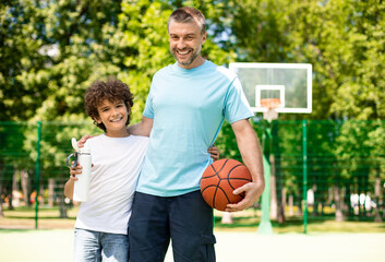 Mature dad hugging little boy who holding basket ball