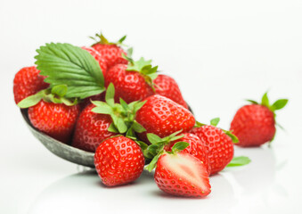 Fresh raw organic strawberries with leaf in steel bowl plate on white background with berries next to it.