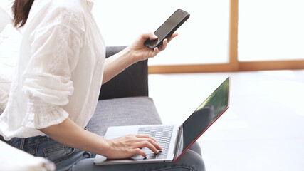 Naklejka premium ソファーでラップトップとスマートンを操作する若い女性