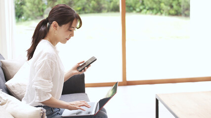 Fototapeta premium ソファーでラップトップとスマートンを操作する若い女性