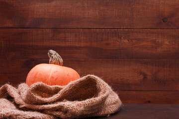 Orange pumpkin, burlap sack against dark brown wooden wall background. Side view, copy space, closeup. Food, autumn, holiday, thanksgiving, harvest season concept.