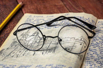 Reading glasses on a vintage travel journal with handwriting and pencil sketches (property release attached) on a rustic wooden table.