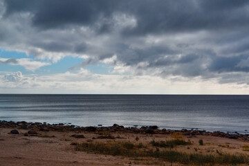 sandy shore with grass on coast of blue Ladoga northern lake at sunset with clouds in sky