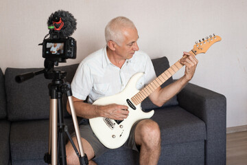 Obraz premium Senior man during quarantine, realizing how important stay at home during virus outbreak. Playing on guitar. Concept of lockdown of coronavirus, self-insulation, healthcare, safety