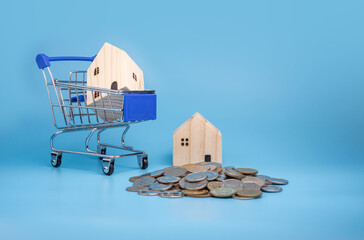 A model wooden house on a shopping cart With a pile of coins.